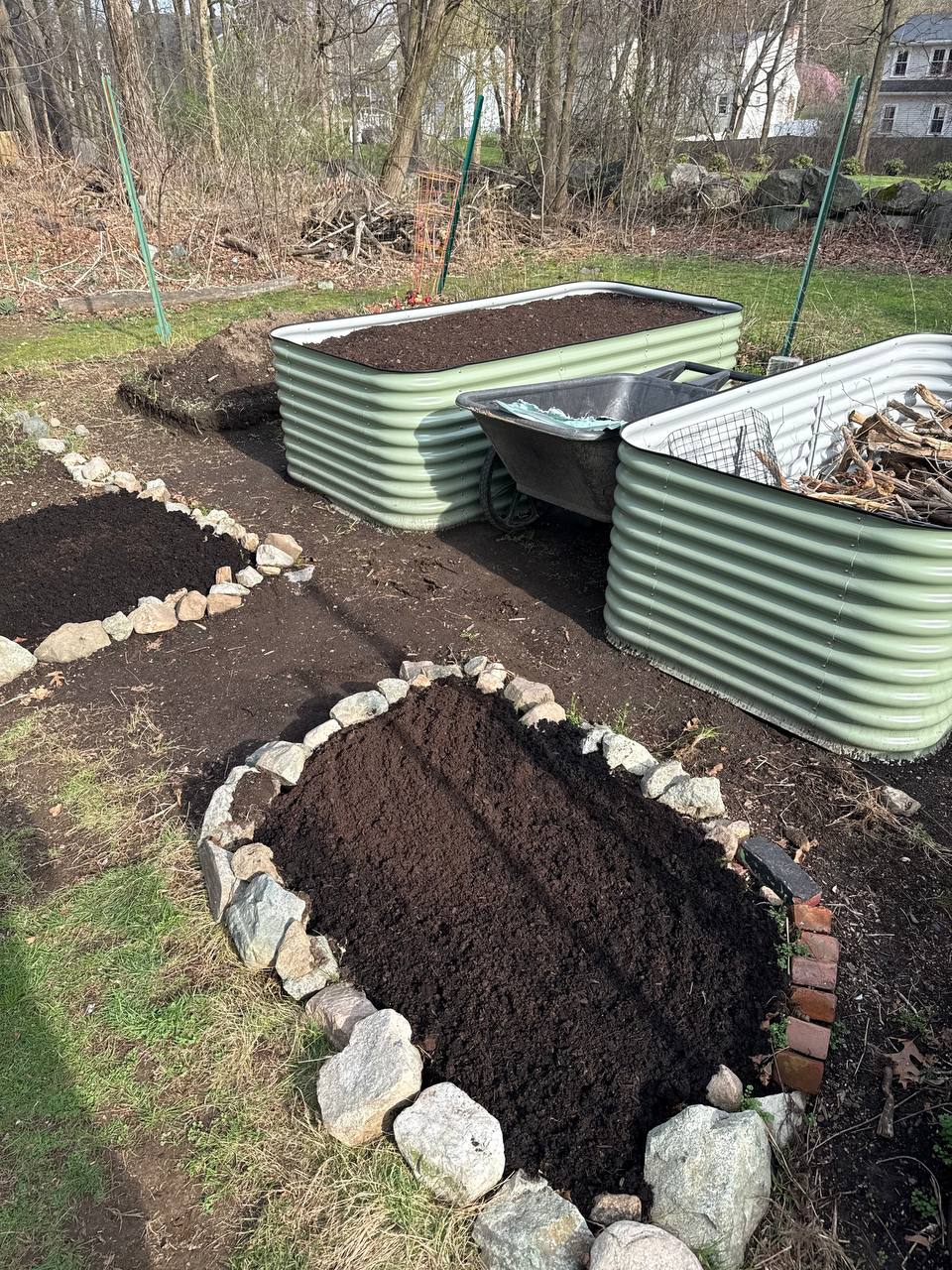 Two Birdies raised beds filled with dark soil, with a circular rock-bordered in-ground bed in the foreground also filled with compost