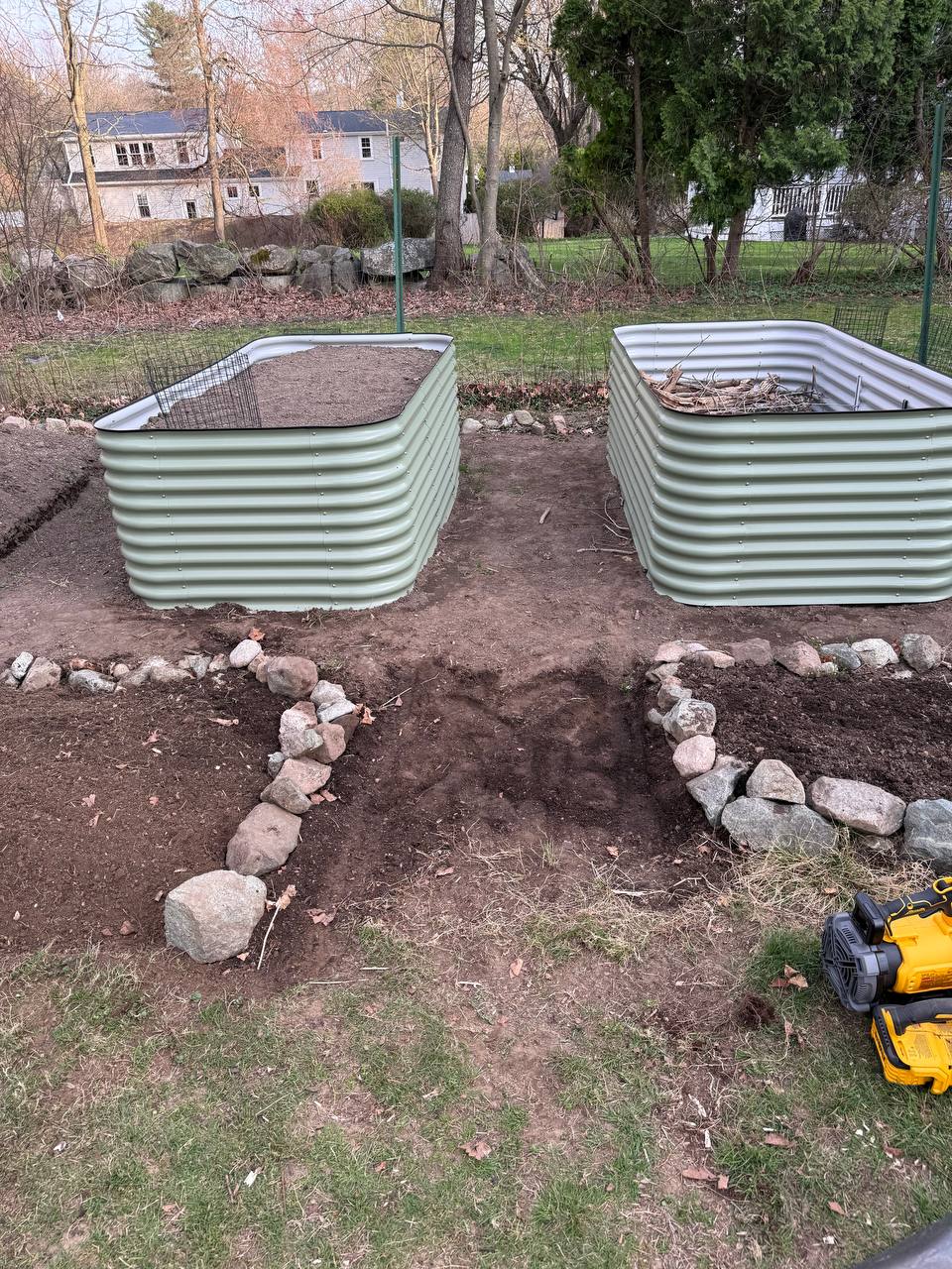 Two Birdies raised beds side by side, one with wire mesh on top and one with branches and sticks as hugelkultur base material