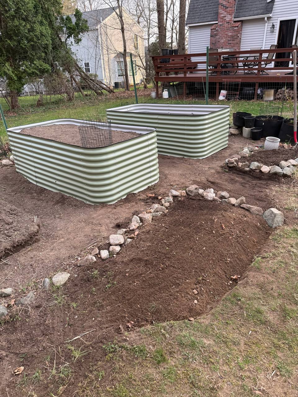 Two Birdies raised beds freshly set up in the backyard with rock-edged pathways and an in-ground bed in the foreground