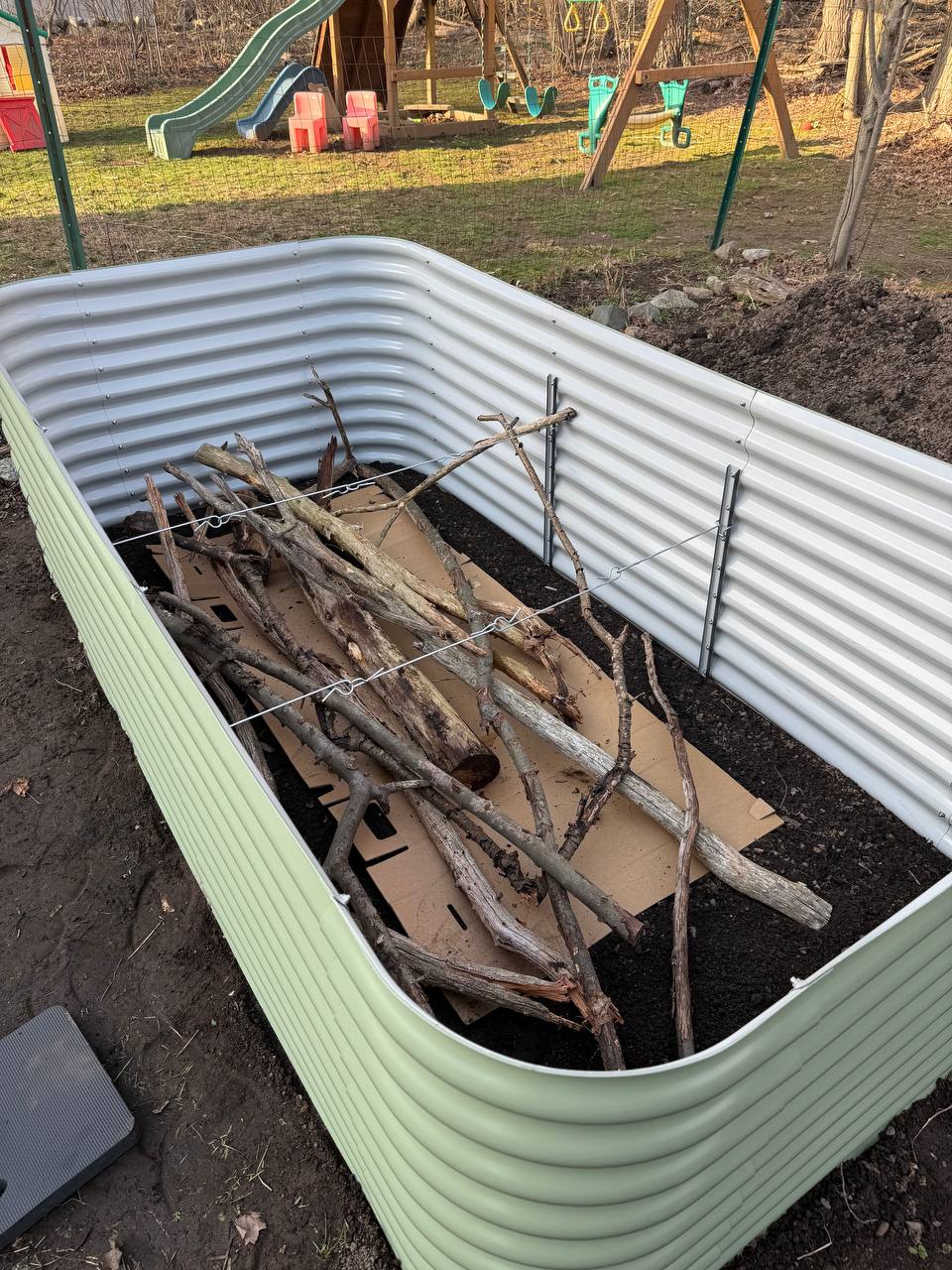 Large logs and branches laid inside a Birdies raised bed over cardboard as the base of a hugelkultur fill