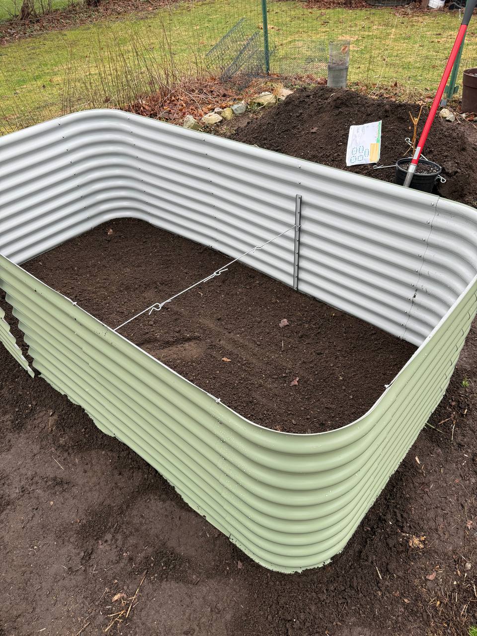 New Birdies raised bed filled with dark soil, with a pile of extra soil behind it and a planting plan visible in the corner